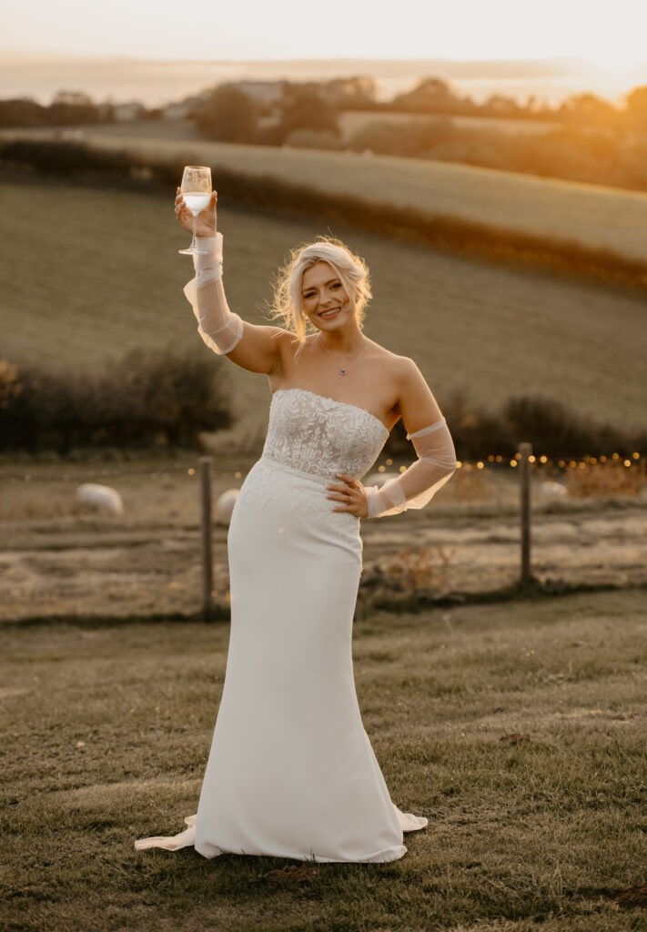 Bride saying cheers with her wine at golden hour at Botley Hill Barn
