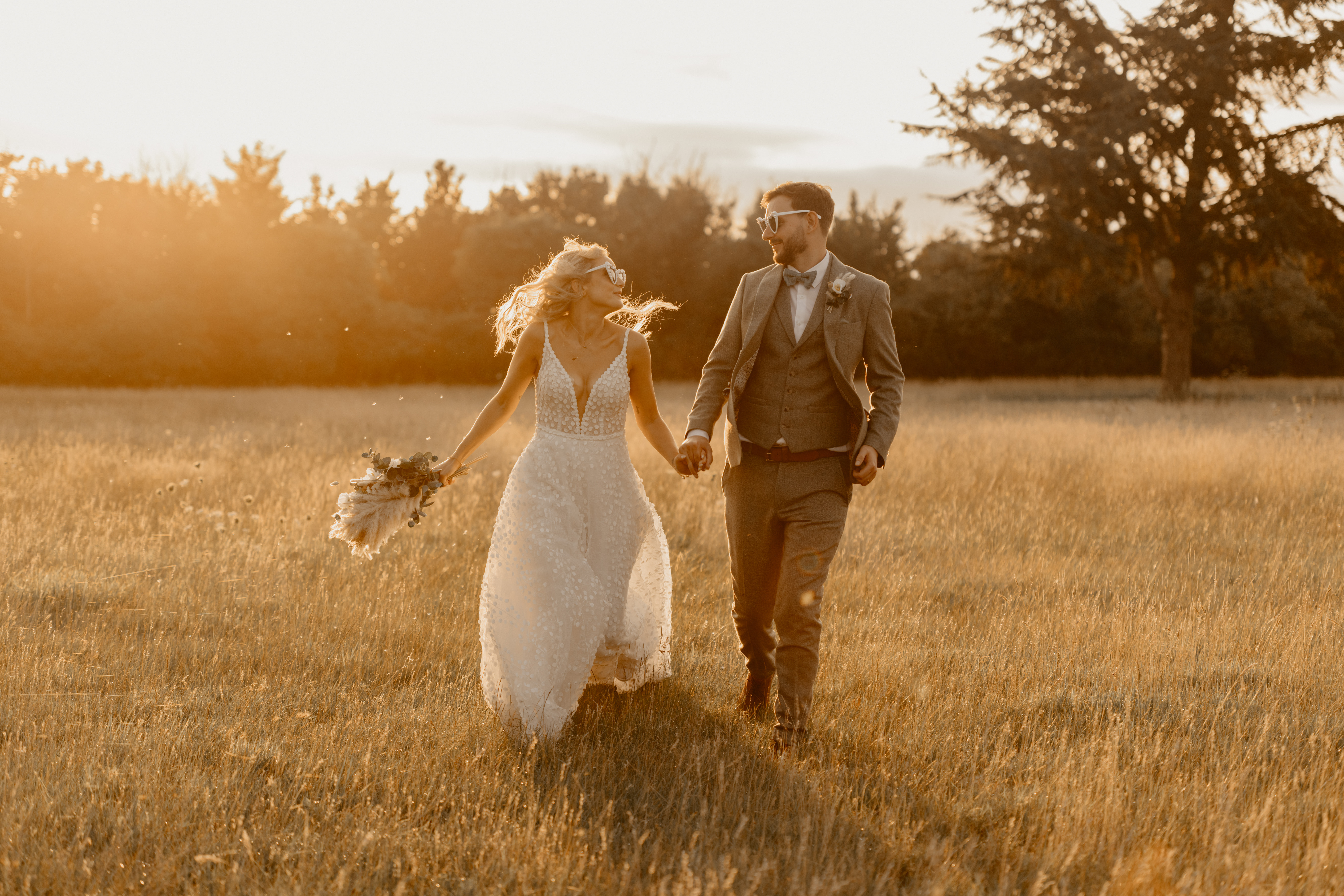 Married couple on their wedding day running through fields at golden hour