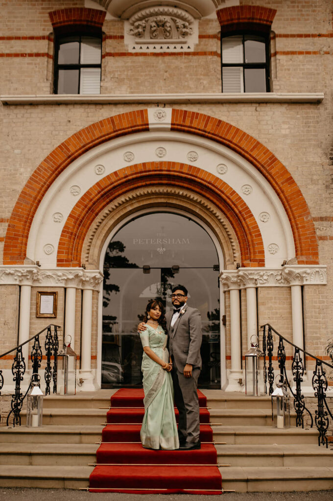 A married couple standing on the steps of the Petersham Hotel