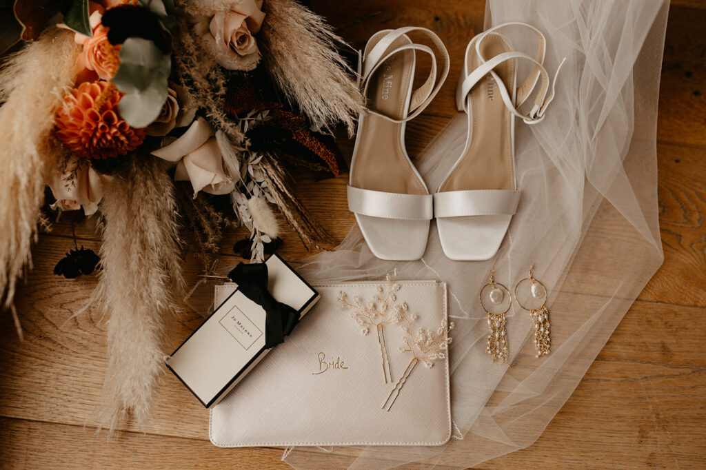Bridal details flatlay with a veil, heels and pampas grass bouquet