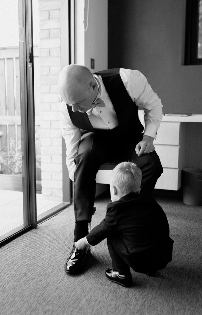 A young boy putting his dad's wedding shoes on