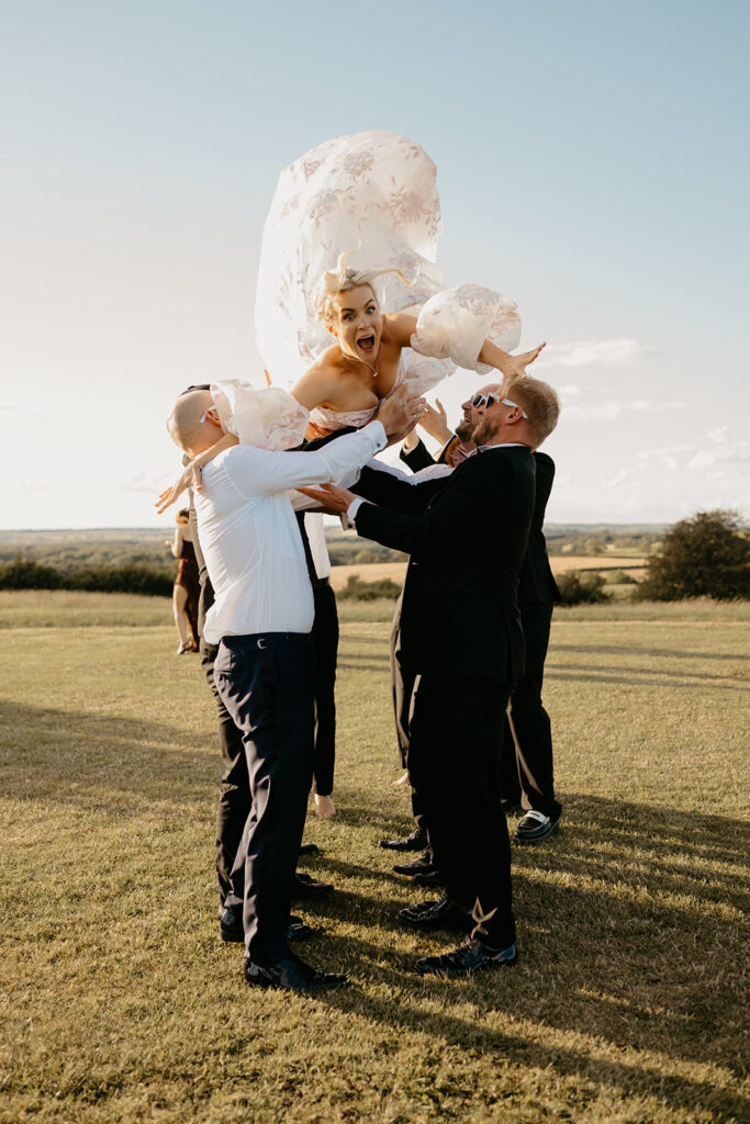 Fun photo of a bride being thrown into the air by the groom and groomsmen
